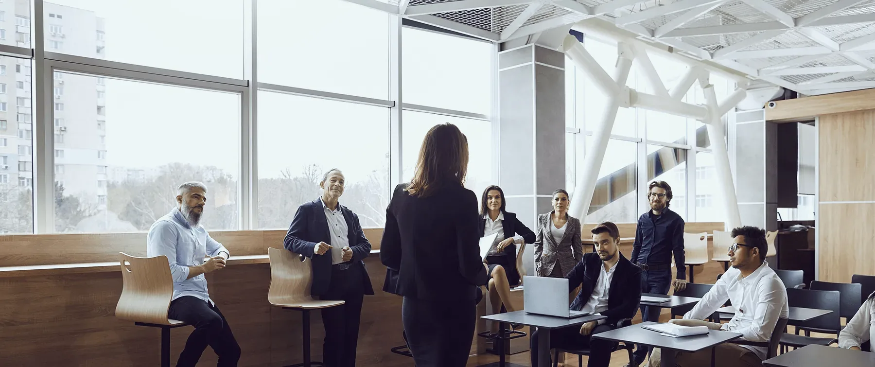A team leader, seen from behind, stands with colleagues working at their desks in a bright office